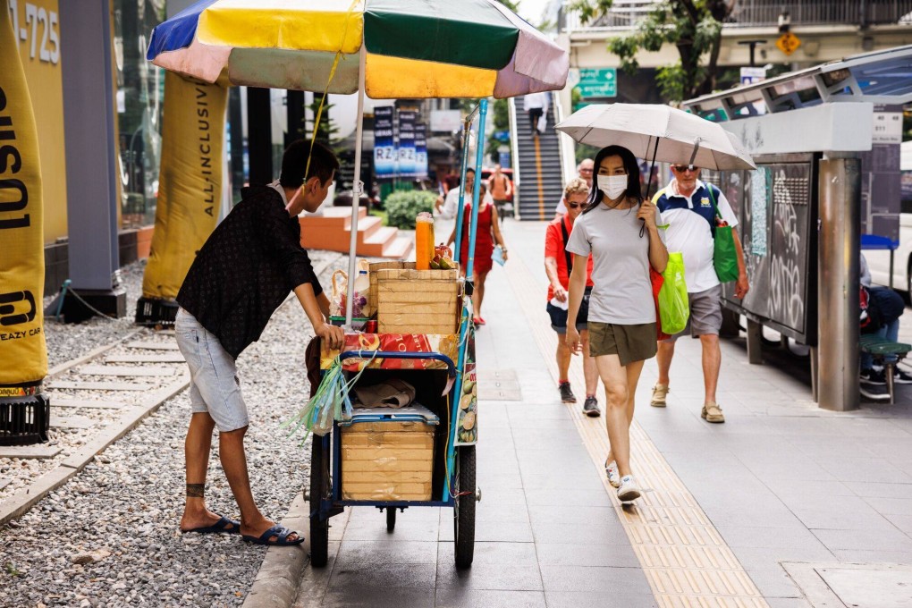 A woman using an umbrella to shade herself from the sun walks past a street vendor selling cold drinks in Bangkok on Tuesday. Photo: Bloomberg