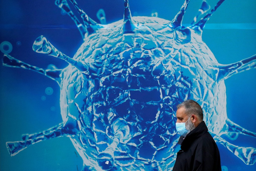 A man wearing a protective face mask walks past an illustration of a virus outside a science centre in the UK. Photo: Reuters