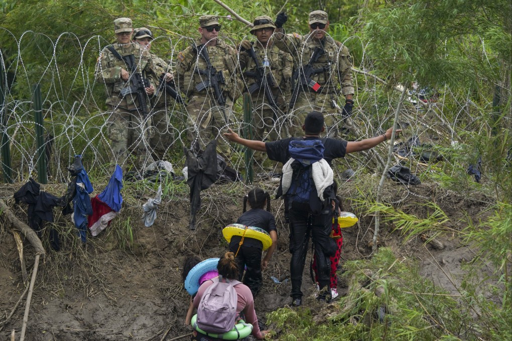 A migrant gestures to Texas National Guards standing behind razor wire on the bank of the Rio Grande river, seen from Matamoros, Mexico, on Thursday. Photo: AP