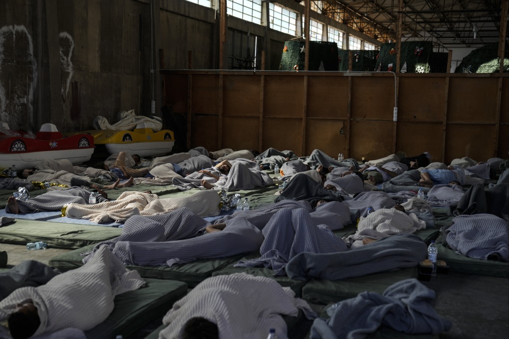 Survivors of the fishing boat that sank sleep on the floor of a warehouse in Kalamata port, Greece. Photo: AP