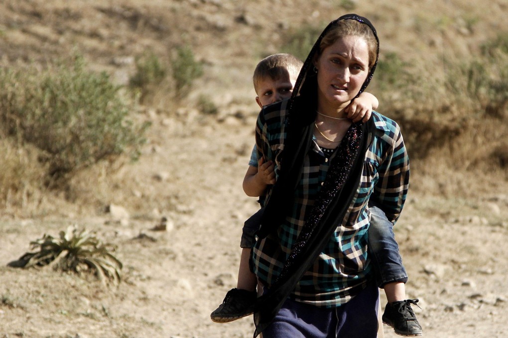 A Yazidi refugee woman carries her son on her back as they flee from Iraq in 2014. Photo: EPA