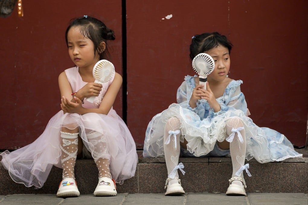 Children cool themselves with electric fans as they take a rest near the Forbidden City in Beijing on Sunday. Photo: AP