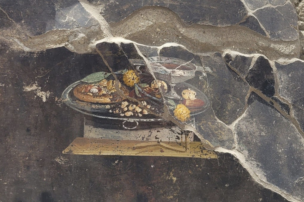 The wall of an ancient Pompeian house with a fresco depicting a table with food. The fresco was found in the atrium of a house in Insula 10 of Regio IX under excavation, to which a bakery was annexed. Photo: Pompeii Archaeological Park via AP