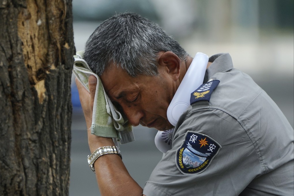 A security guard wearing an electric fan on his neck wipes his sweat on a hot day in Beijing on Monday. Photo: AP