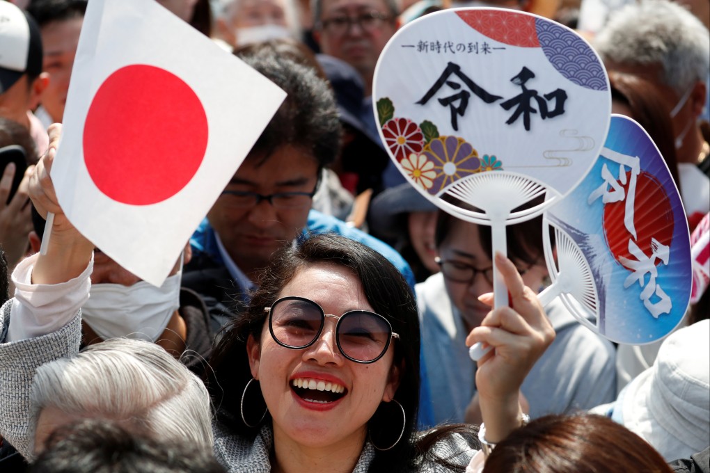 A woman waves a Japanese flag and a paper fan bearing the name of the new imperial era, “Reiwa”, before the first public appearance of Emperor Naruhito and Empress Masako at the Imperial Palace in Tokyo in 2019. The characters for “Reiwa” are translated as “beautiful harmony”. Photo: Reuters