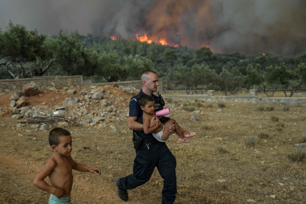 A Greek policeman evacuates children from wild fire in a village near the capital Athens as Europe braces for new high temperatures that have scorched swathes of the Northern Hemisphere. Photo: AFP