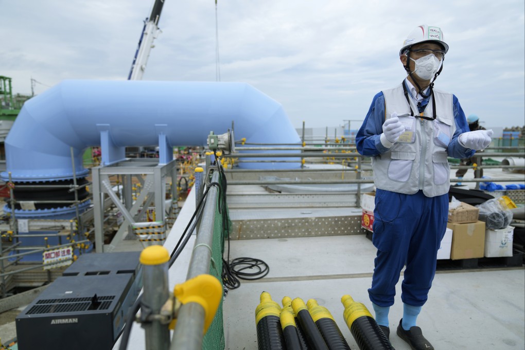 A Tepco spokeman speaks during a tour of the Fukushima Daiichi nuclear power plant on July 14. He says treated radioactive water will be diluted with more than hundred times the seawater in this blue pipe, background, to levels much safer than international standards, before released into the sea. Photo: AP