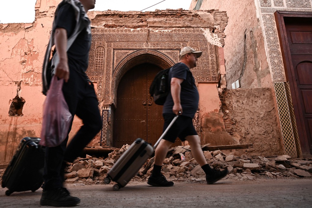 Tourists drag their suitcases as they walk past a damaged building in the old quarter of Marrakech, two days after an earthquake in mountains nearby caused widespread damage and killed more than 2,000 people. Some tourists have decided not to flee the city. Photo: TNS