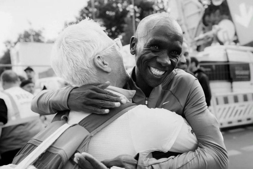 Eliud Kipchoge and Claus-Henning “Bottle Claus” Schulke embrace. Bottle Claus has become a star in the running world for his perfect nutrition bottle handoffs and fist-pump celebration, but what makes the 57-year-old Berliner so good at what he does? Photo: Instagram/@bottle_claus