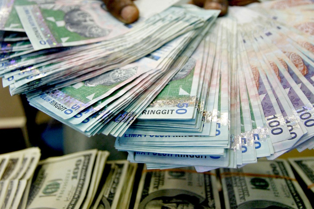 A money changer holds out Malaysian ringgit banknotes above stacks of US$100 bills at a foreign-exchange counter in Kuala Lumpur. Photo: AFP