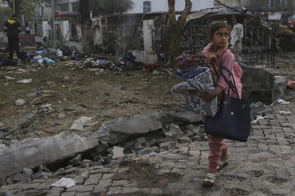 A Palestinian girl carries blankets as she walks past the site of a deadly explosion at the Al-Ahli Hospital in Gaza City on October 18. Photo: AP