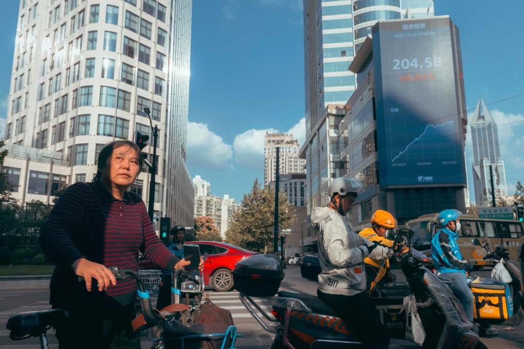 People riding bicycles and scooters on the street beneath a screen showing the latest stock and economy data in Shanghai in October 2023. Photo: EPA-EFE