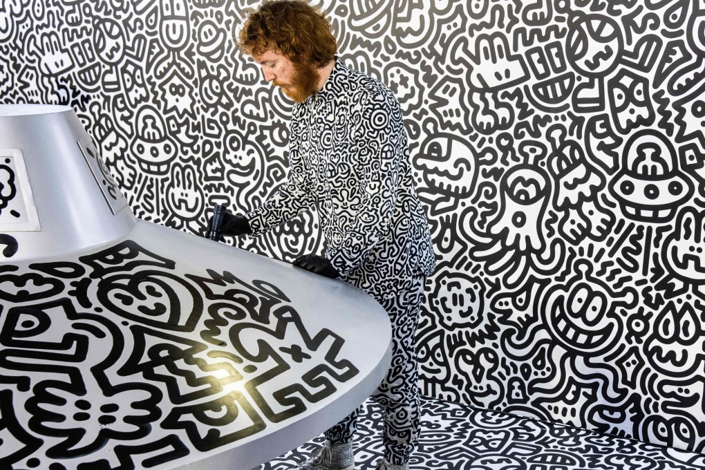 British artist Sam Cox, better known as Mr Doodle, draws on a model spaceship at Hong Kong MTR station in Central, Hong Kong on November 19. His work is on show at a shopping centre in Kowloon and an art gallery in Central. Photo: AFP