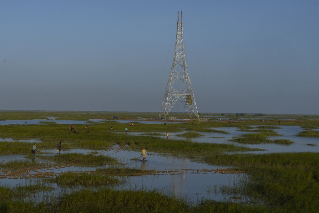 Workers walk through a swamp to install electric transmission towers for the Adani Renewable Energy Park near Khavda, Bhuj district, near the India-Pakistan border in Gujarat, India, in September. India is developing a 30 gigawatt hybrid — wind and solar — renewable energy project on one of the largest salt deserts in the world. Photo: AP