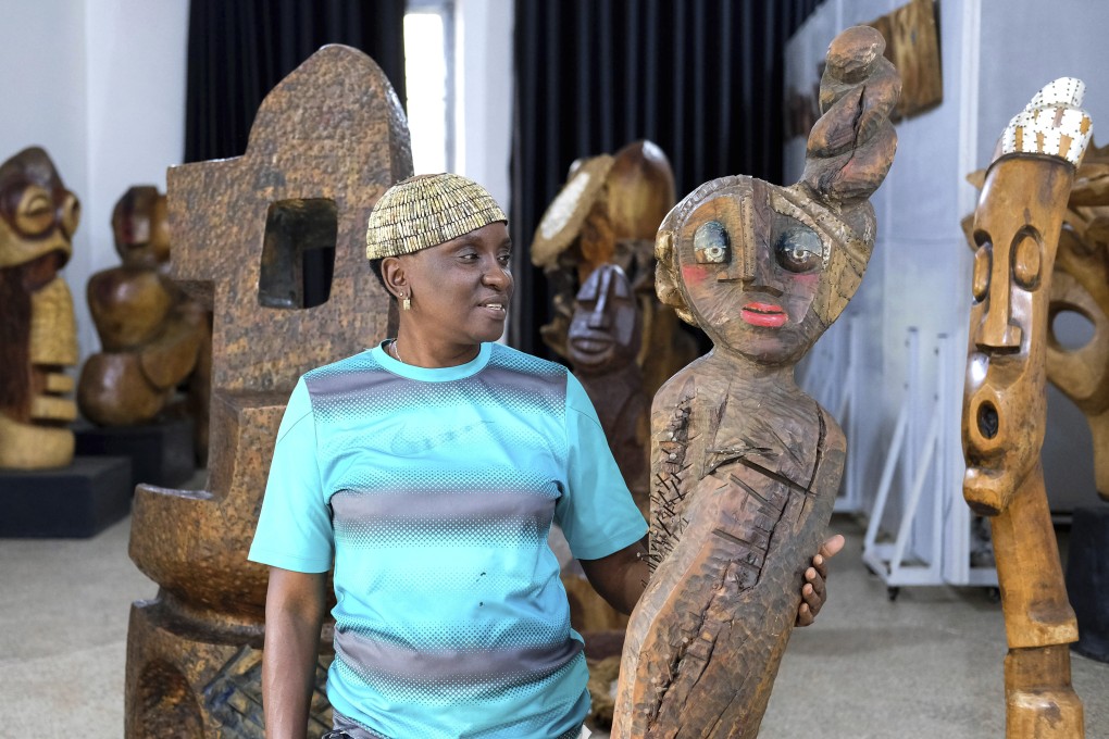 Lilian Nabulime stands next to a wooden sculpture piece at her workshop in Kyanja, a suburb in Kampala City, Wednesday Nov. 29 2023. Lilian Nabulime hasn’t forgotten the time in the 1990s when the Ugandan capital had just one commercial art gallery, a small space that emerging artists struggled to get into. Now there are at least six in Kampala, including one whose curators recently exhibited the sculptor’s contrarian work. (AP Photo/Hajarah Nalwadda.)