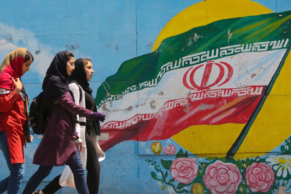 Young girls walk in front of a mural showing the Iranian national flag in the center of the  capital Tehran. Photo: TNS