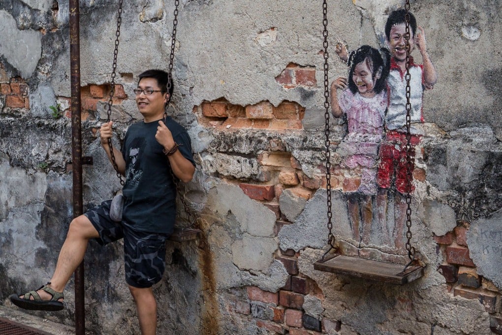 A tourist has his photo taken next to “Brother and Sister on a Swing”, a work of street art in George Town, Penang, Malaysia, by local artist Louis Gan. Photo: Getty Images