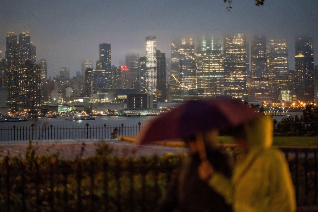 People walk in the rain while the New York skyline is covered with clouds during a coastal storm on September 29, 2023, as seen from Weehawken, New Jersey. The US, the largest commercial property market in the world, has seen prices tumble since the Federal Reserve started raising interest rates. Photo: AFP