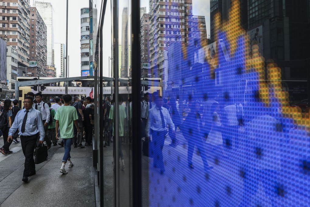 People walking near a screen showing the Hang Seng Index chart outside a bank branch in Mong Kok, hong Kong. Photo: Sam Tsang