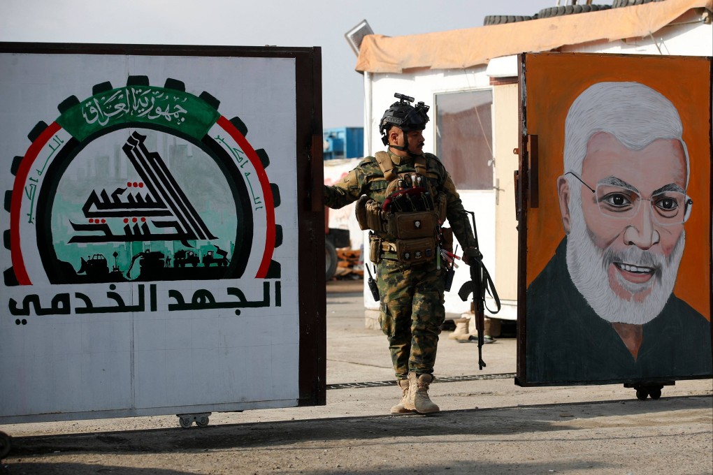 A member of Iraq’s Popular Mobilisation Forces stands guard at the gate of the paramilitary forces’ headquarters, between their logo and a portrait of slain leader Abu Mahdi al-Mohandis, ahead of the funeral of people killed the previous day in US strikes in western Iraq. Photo: AFP