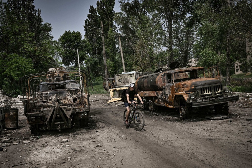 A man rides his bicycle between two destroyed military trucks in the city of Lysychansk in the Donbas region on June 11, 2022. Photo: AFP