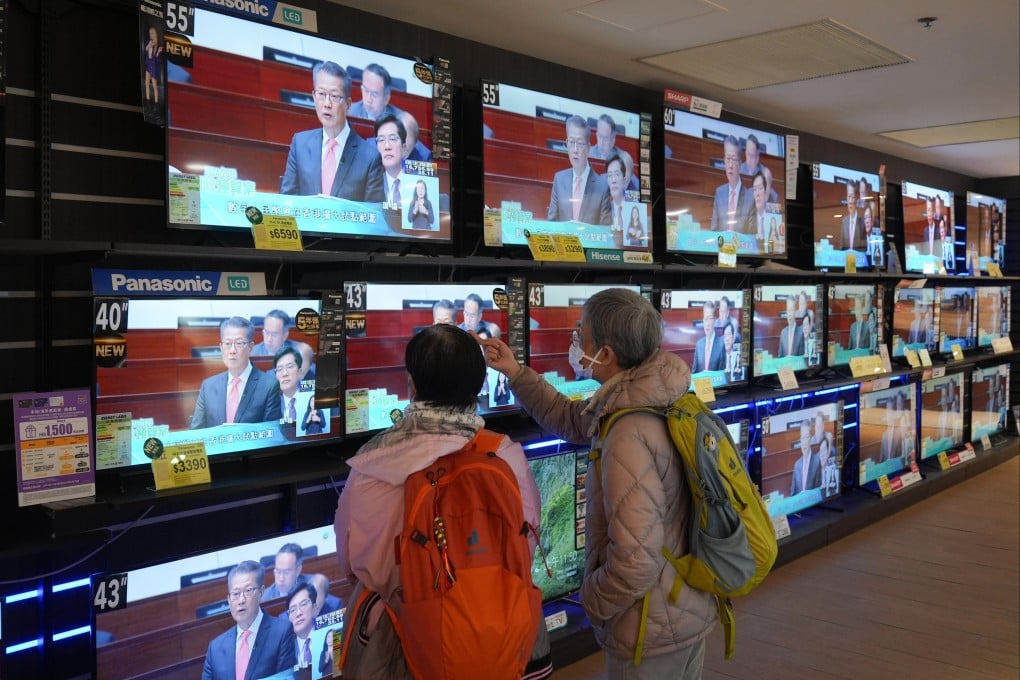 Residents watch Paul Chan’s address on television. Consumption vouchers are among the sweeteners to have been scrapped. Photo: Eugene Lee