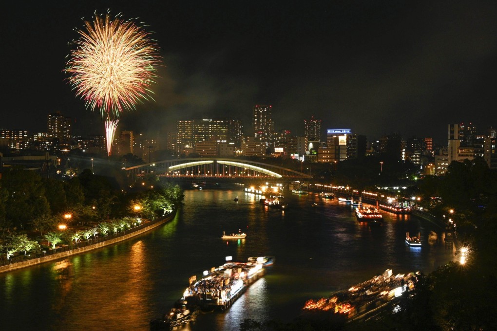 Boats sail along a river in Osaka, Japan during the Tenjin Festival on July 25, 2023, with fireworks lighting up the night sky. Photo: Kyodo