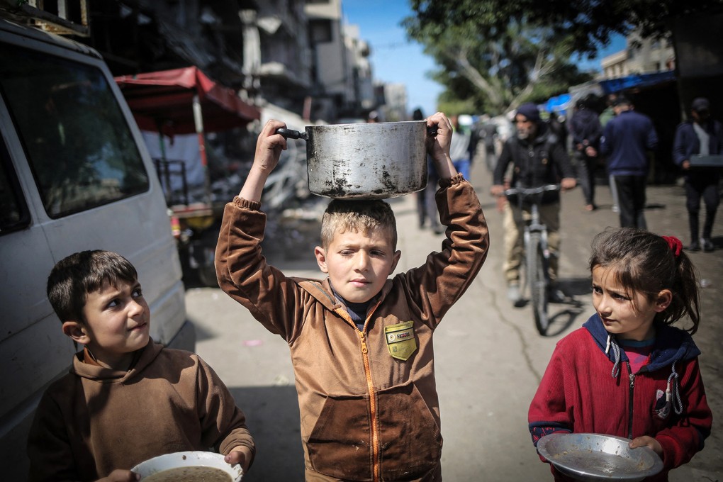 Children carry kitchen utensils as they walk towards a food distribution point in Khan Younis in the southern Gaza Strip on March 7. Photo: TNS
