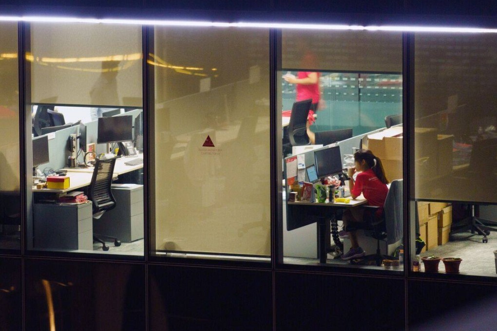 Office workers are seen at night through the windows of a commercial building in the central business district of Singapore. Photo: Bloomberg