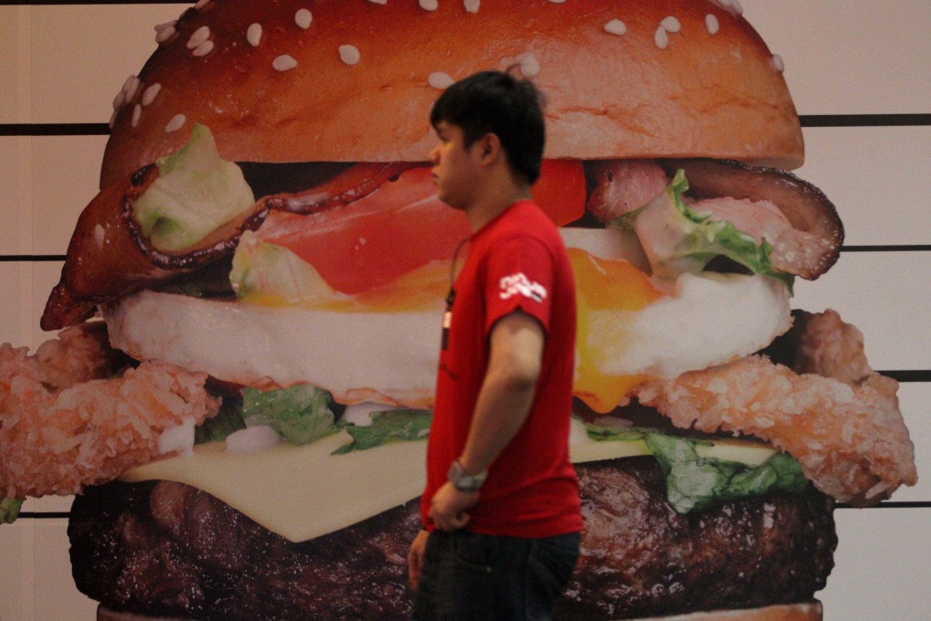 A worker walking past a burger advertisement poster inside a restaurant in Kuala Lumpur. Photo: AFP
