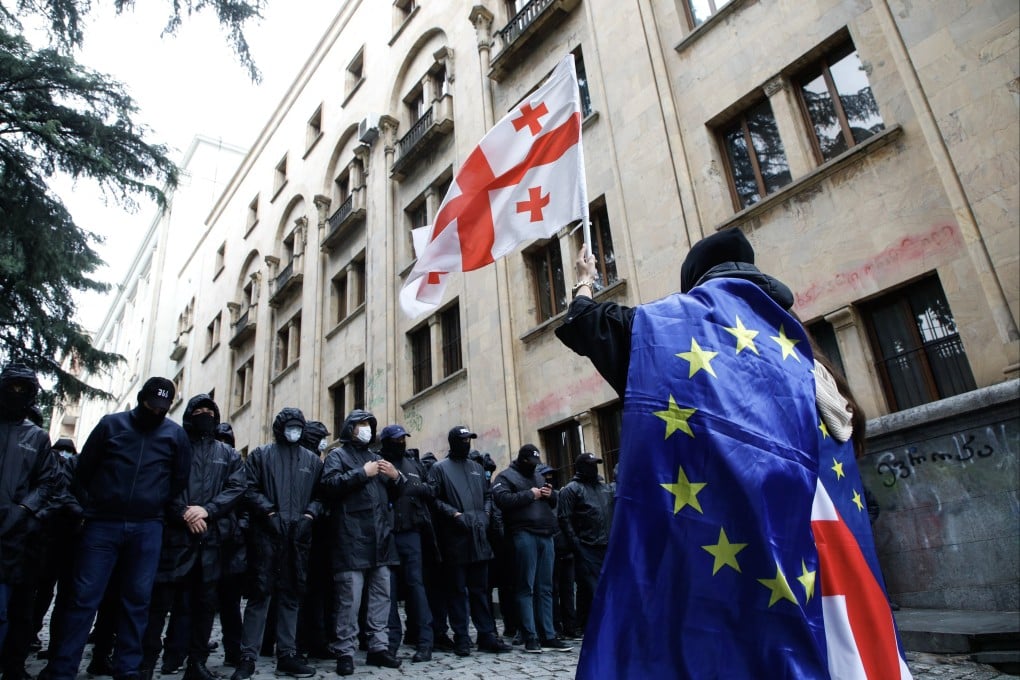 A protester waves a Georgian flag while wearing the European flag in front of policemen blocking a street during a rally against a draft bill on ‘foreign agents’ near the Parliament building in Tbilisi, Georgia on Tuesday. Photo: EPA-EFE