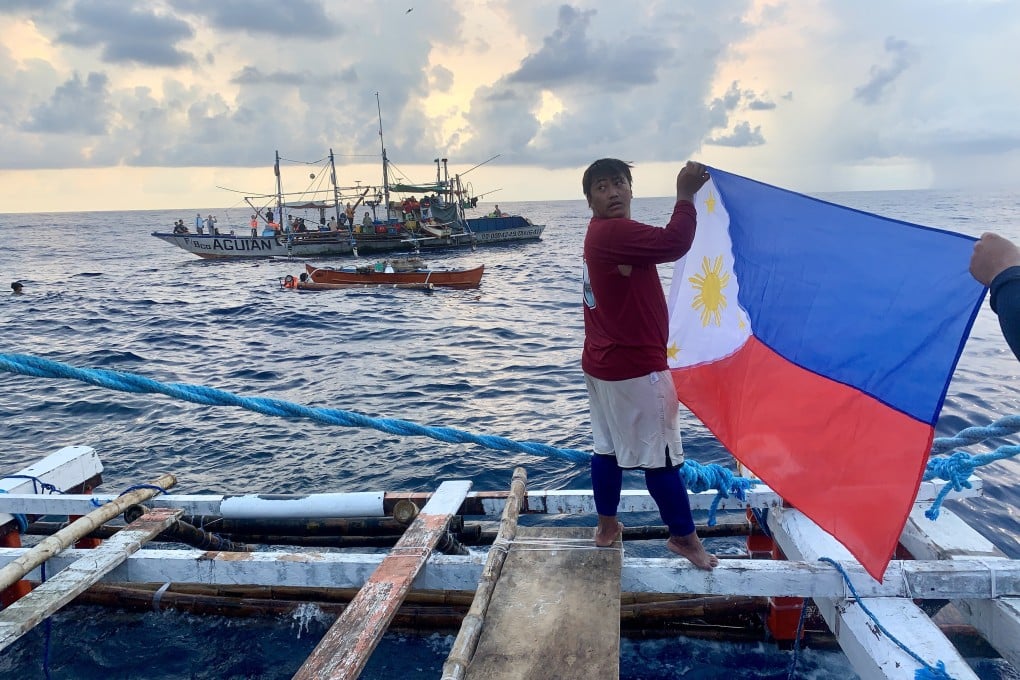 A Filipino fisherman waves a Philippine flag aboard a wooden boat as they sail towards Scarborough Shoal in the disputed South China Sea. Photo: EPA-EFE