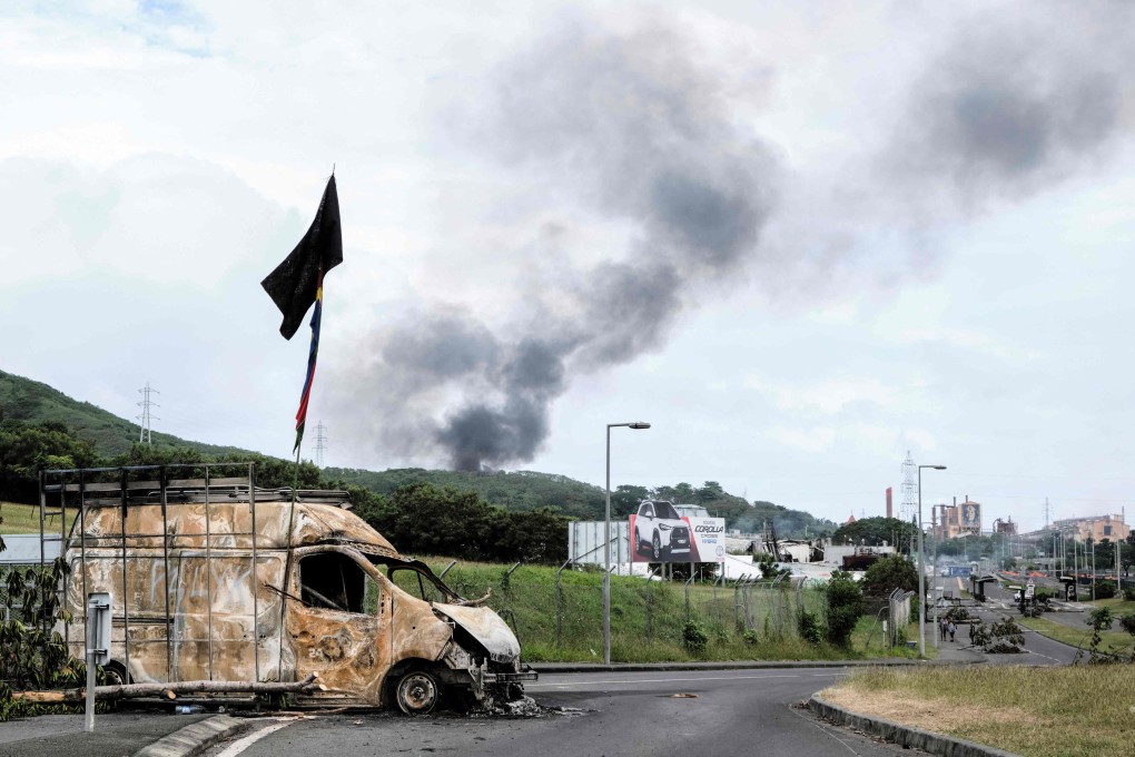 Smoke rises in the distance as a burnt-out vehicle and roadblock barricades are seen on a road near the Montravel area of Noumea in New Caledonia on Tuesday. Photo: AFP