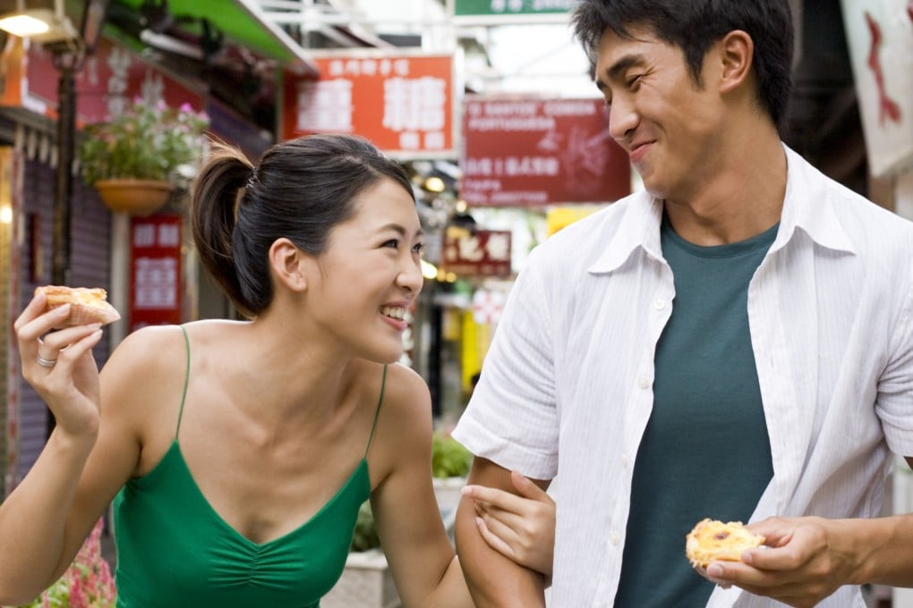 Young couple enjoying snacks on the streets of Macau., The city’s culinary heritage comes to the fore at International Cities of Gastronomy Fest, celebrating the SAR’s 25th anniversary and its status as a City of Gastronomy. Photo: Getty Images