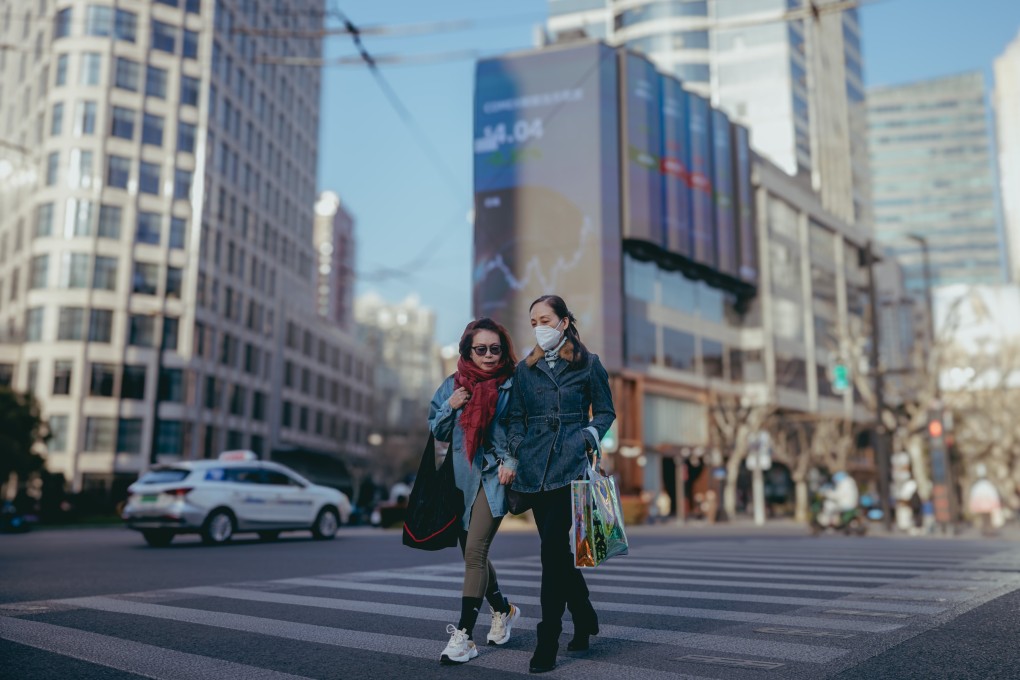 People cross a street near a large screen showing stock exchange data in Shanghai on March 20, 2024. Photo: EPA-EFE