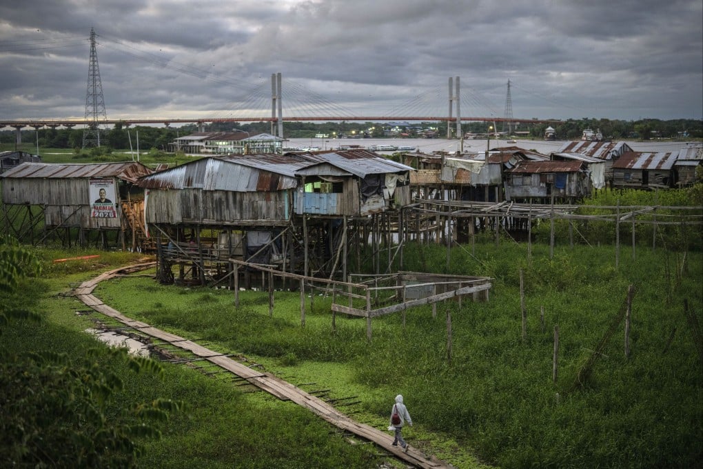 A highway bridge (in background) that is part of a federal highway project, extends across the Nanay River as a resident walks along a boarded path in the Punchana district of Iquitos, Peru. Photo: AP