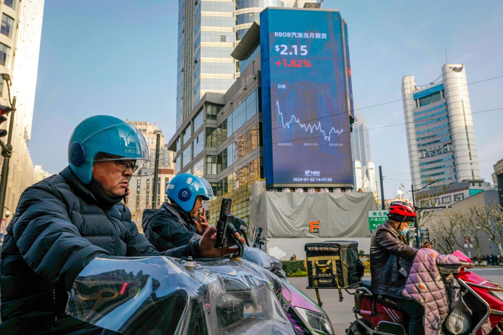 People ride scooters on the street beneath a large screen showing the latest stock data in Shanghai on January 2, 2024. Photo: EPA-EFE