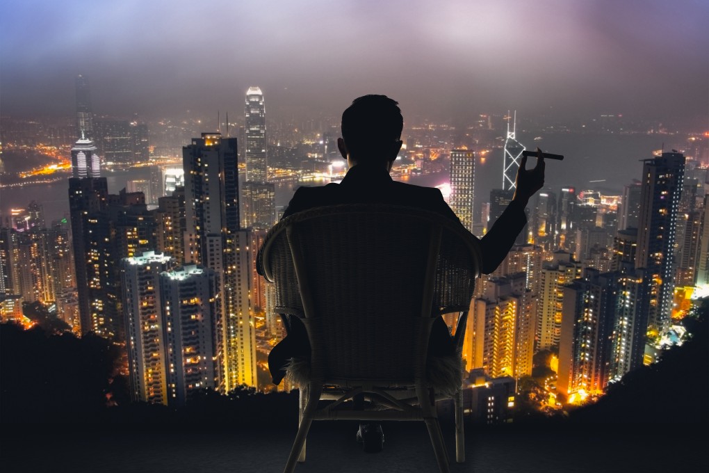 Silhouette of a businessman sitting on a chair and holding a cigar, overlooking the city of Hong Kong. The city recorded a dip in its population of wealthy citizens, according to a report by Altrata. Photo: Shutterstock