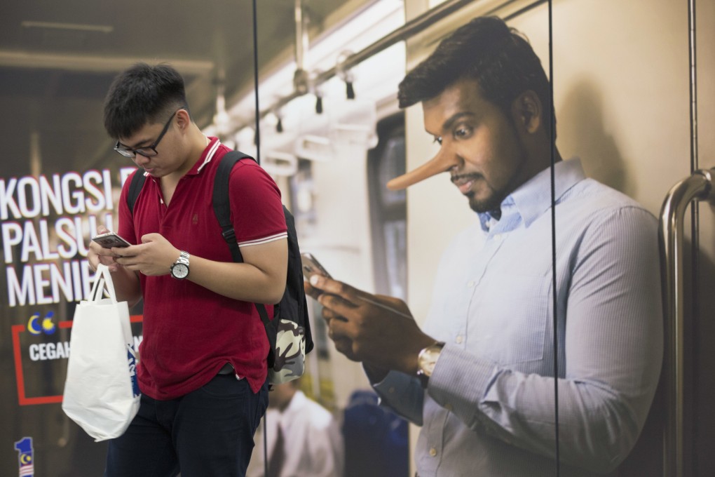 A commuter reads from his mobile phone next to an advertisement discouraging the dissemination of fake news at a train station in Kuala Lumpur, Malaysia. File photo: AP