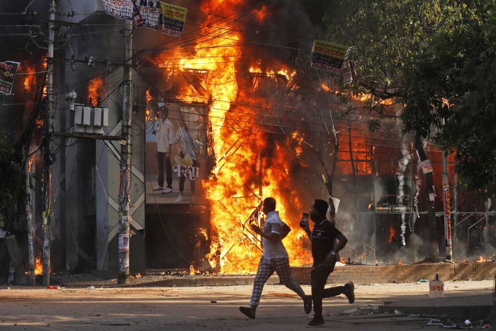 Men run past a shopping centre which was set on fire by protesters in Dhaka, Bangladesh. Photo: AP