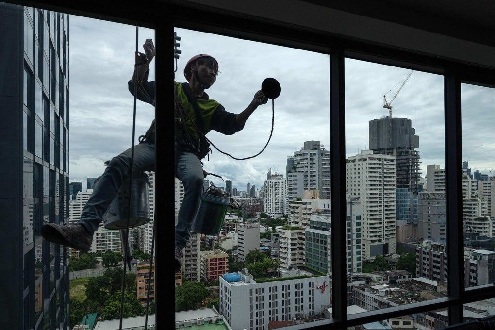 A worker repairs the window of an apartment in Bangkok. Thailand’s development is concentrated mainly in the capital and other major cities. Photo: AFP