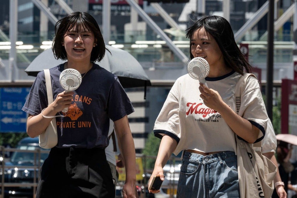 Young women using portable fans to seek relief from the heat while walking outside Tokyo’s Shinjuku station. Photo: AFP