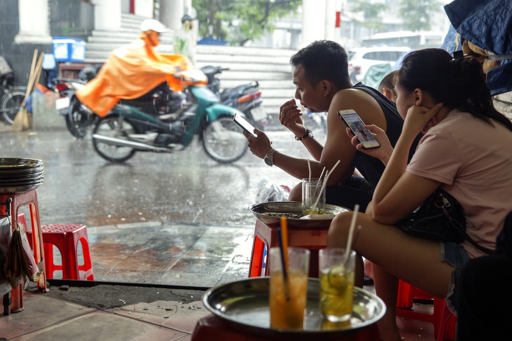 People use smartphones as they drink tea by a road in Hanoi. Photo: Bloomberg