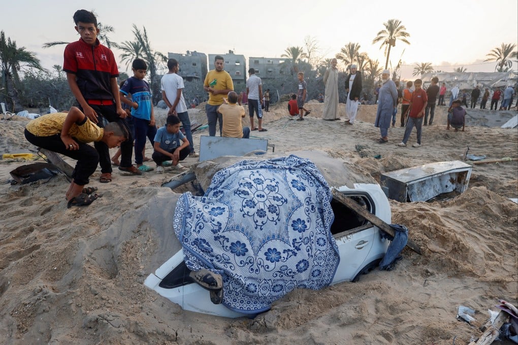 Palestinian boys stand near a buried damaged vehicle following Israeli strikes on a tent camp. Photo: Reuters