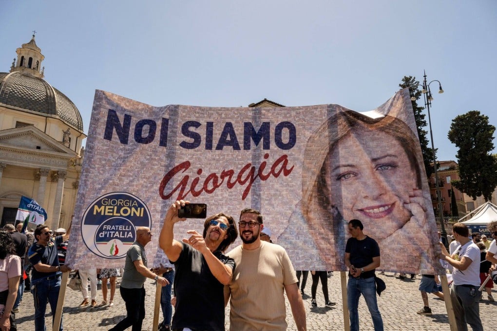 Attendees pose in front of a banner featuring Italy Prime Minister Giorgia Meloni at a Brothers of Italy party rally. Photo: Bloomberg