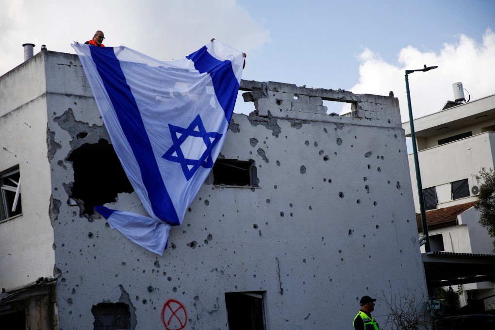 Men hang an Israeli flag over a damaged building in Kiryat Bialik, Israel. Photo: Reuters