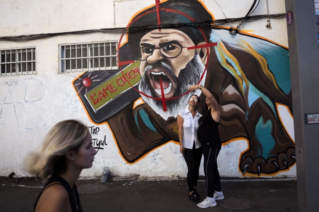 Two women take a selfie next to a newly painted graffiti of Hezbollah leader Hassan Nasrallah in Tel Aviv, Israel. Photo: AFP