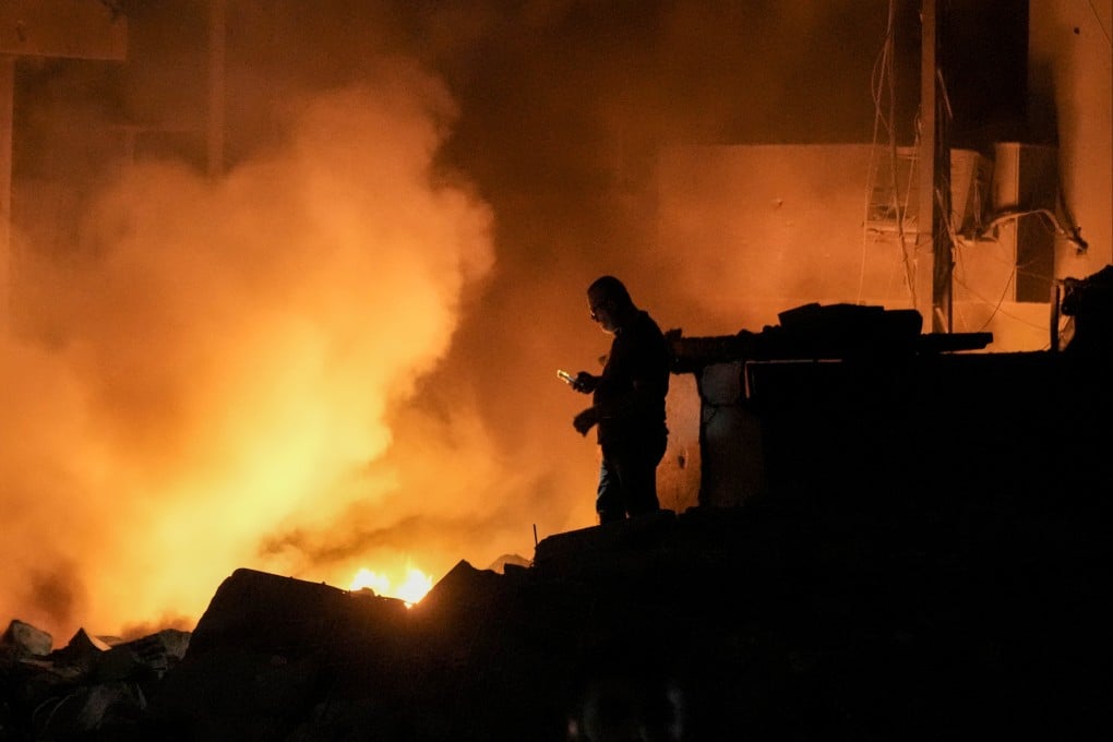 A man uses his mobile phone as flames and smoke rise at the site of buildings hit by an Israeli strike in central Beirut, Lebanon on Thursday. Photo: AP