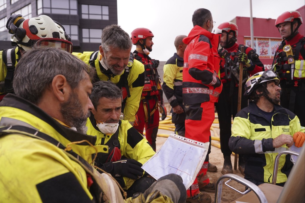 Rescue workers look at a plan of a Valencia shopping centre on Monday as the search for bodies continues after devastating floods. Photo: AP