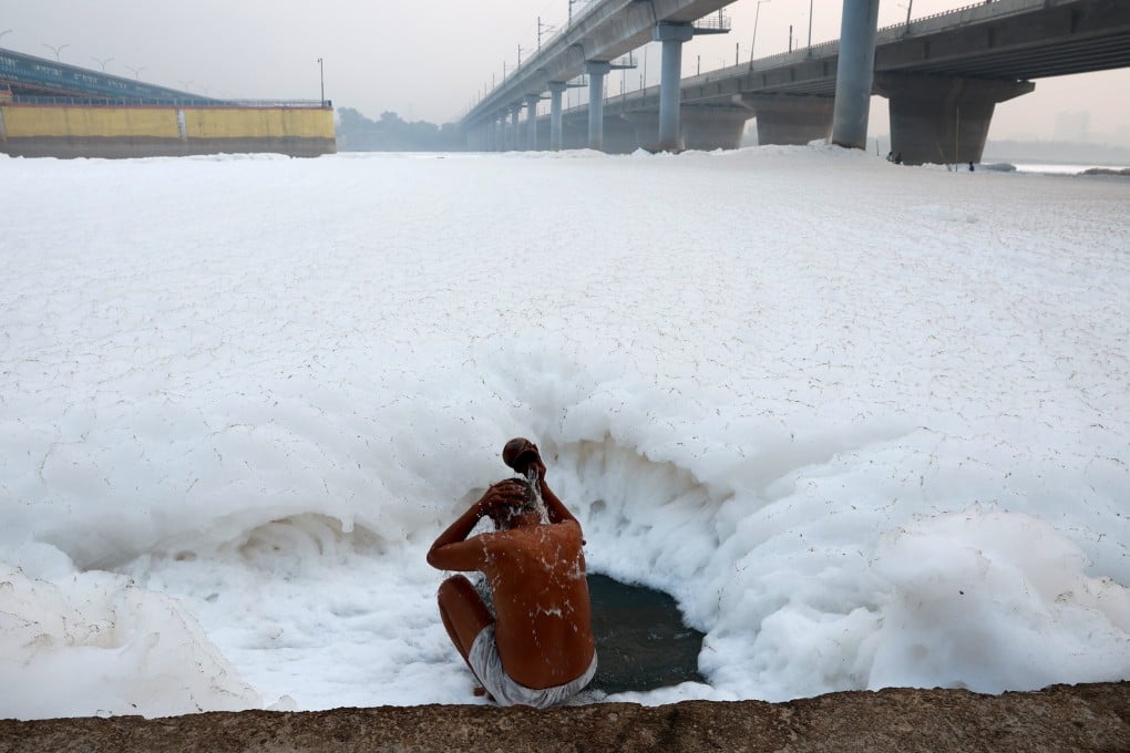 A man bathes himself while toxic foam caused by industrial waste floats on the surface of the Yamuna river in New Delhi. Photo: EPA-EFE